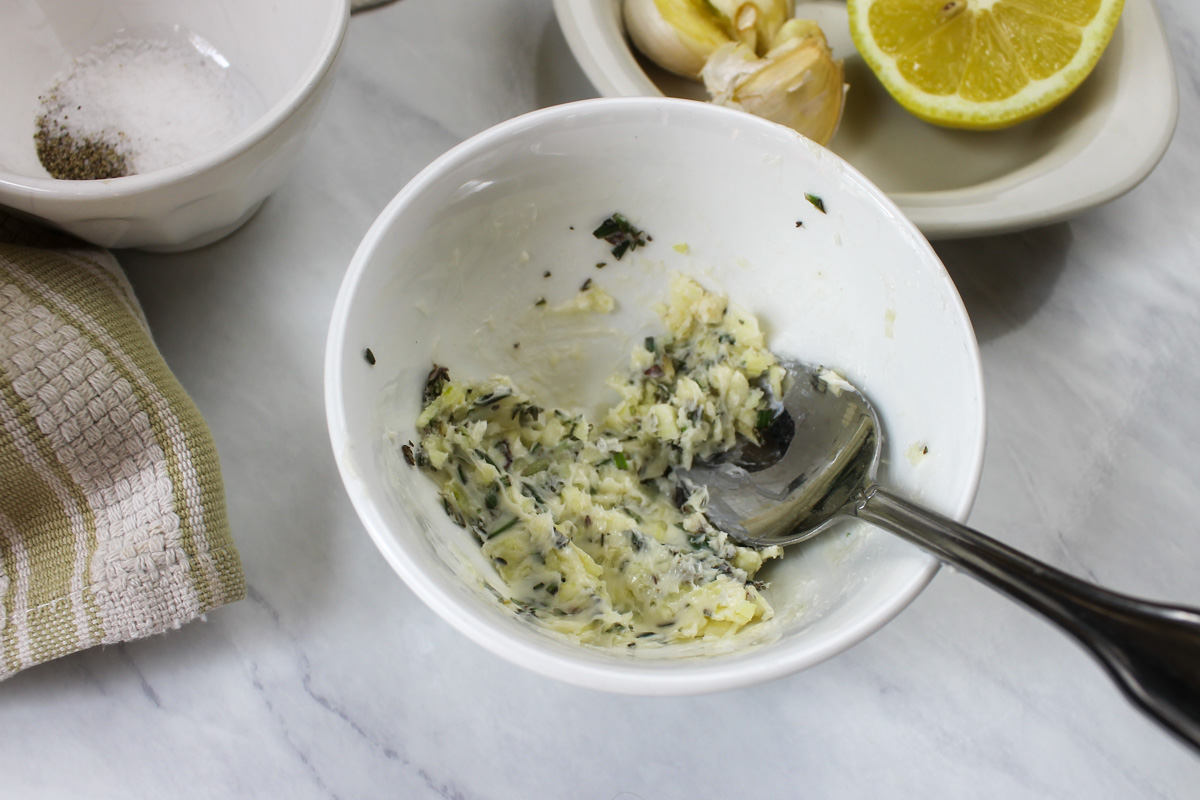 A small white bowl of garlic herb butter to coat a whole chicken.