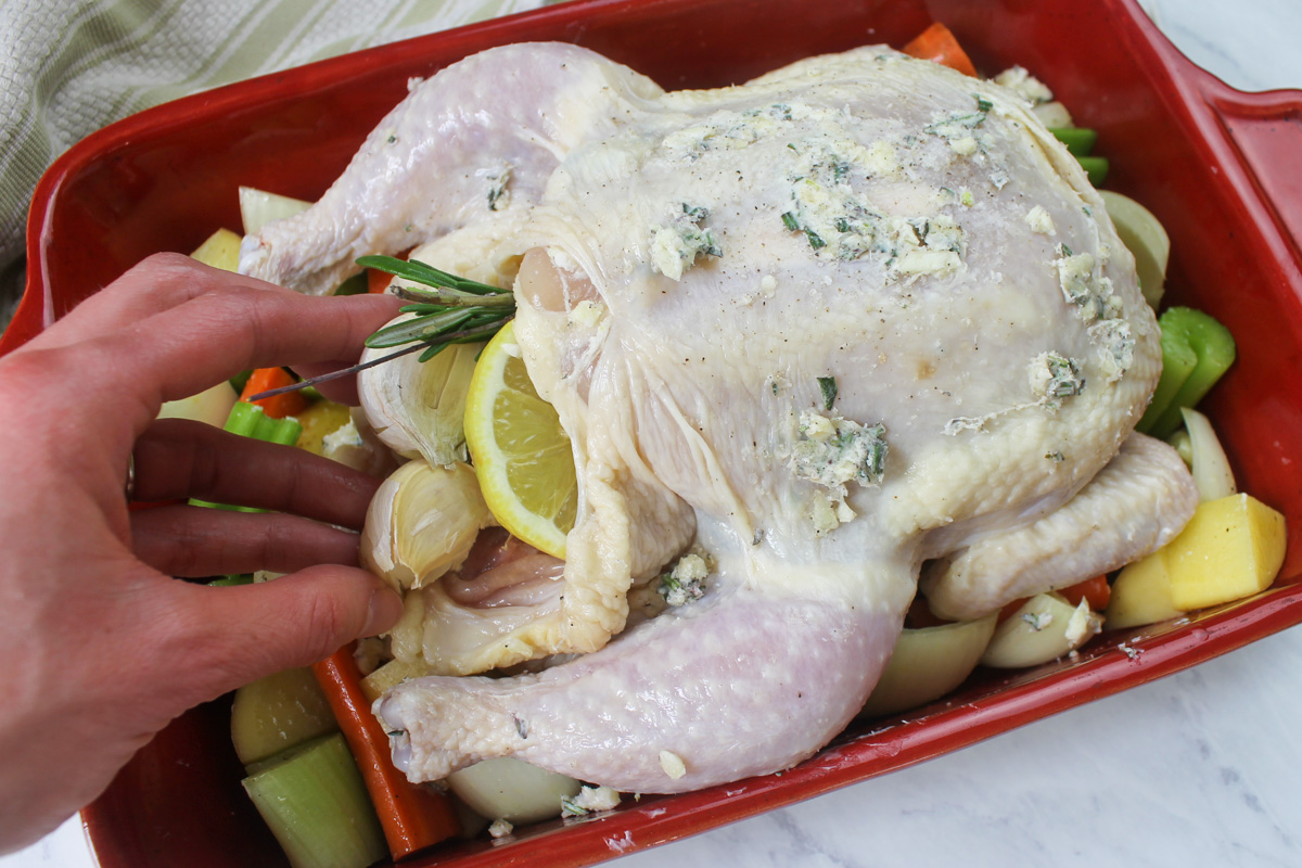 Adding garlic, lemon, and rosemary to the cavity of a raw whole chicken.