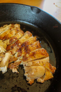 Seared and roasted chicken breasts, sliced and in a cast iron pan.