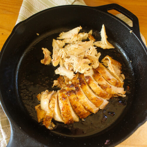 A cast iron skillet with sliced bone-in skin-on chicken breast.