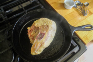 Raw chicken breast searing skin side down in a cast iron skillet.