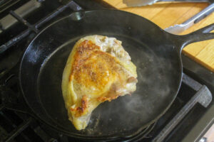 Chicken breast searing in a cast iron skillet.