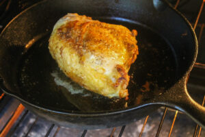 A chicken breast finishing cooking in the oven after being seared on the stove in a skillet.