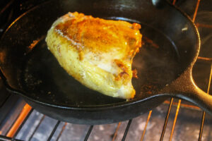 Chicken breast in a cast iron skillet being transferred to the oven to finish cooking.