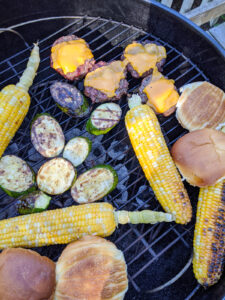 A grill with charred corn on the cob, burgers and grilled zucchini.