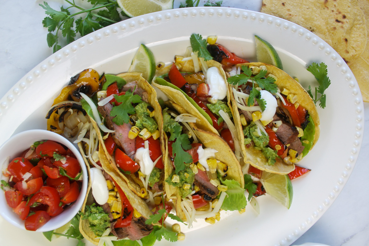 A platter of assembled steak fajitas with a bowl of pico de gallo salsa.