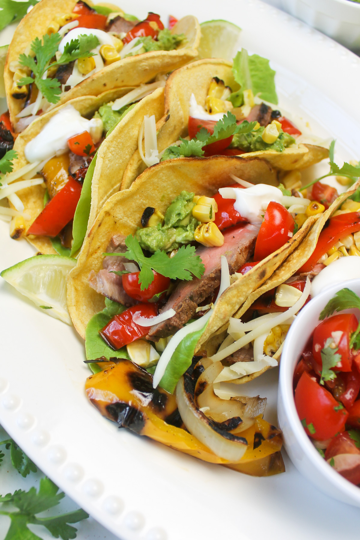 Steak fajita tacos on a platter with lots of toppings.