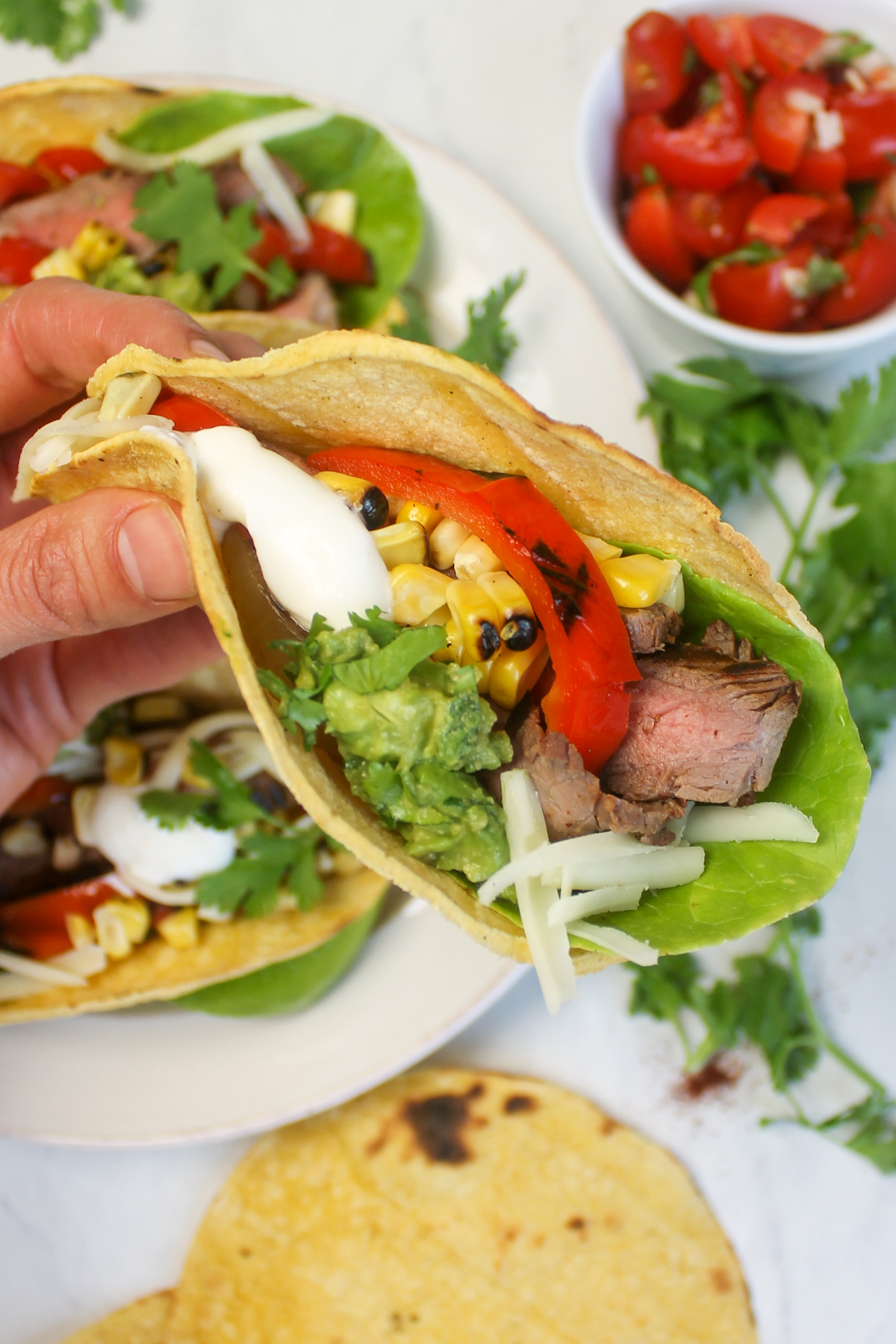 A hand holding a steak fajita taco with charred corn.