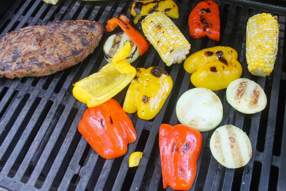 Grilling steak, peppers, onions and corn on an outdoor grill for fajitas.