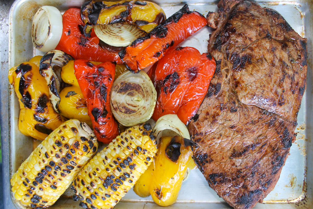 Grilled steak and charred corn, peppers and onions on a sheet pan.