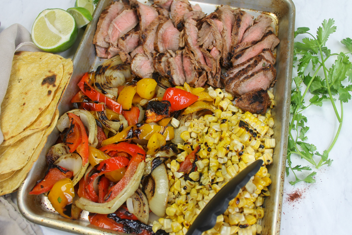 Grilled fajita ingredients sliced on a sheet pan ready to assemble into tacos.