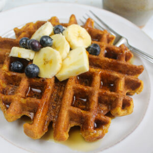 Pumpkin oat waffles with banana and blueberry topping on a white plate.
