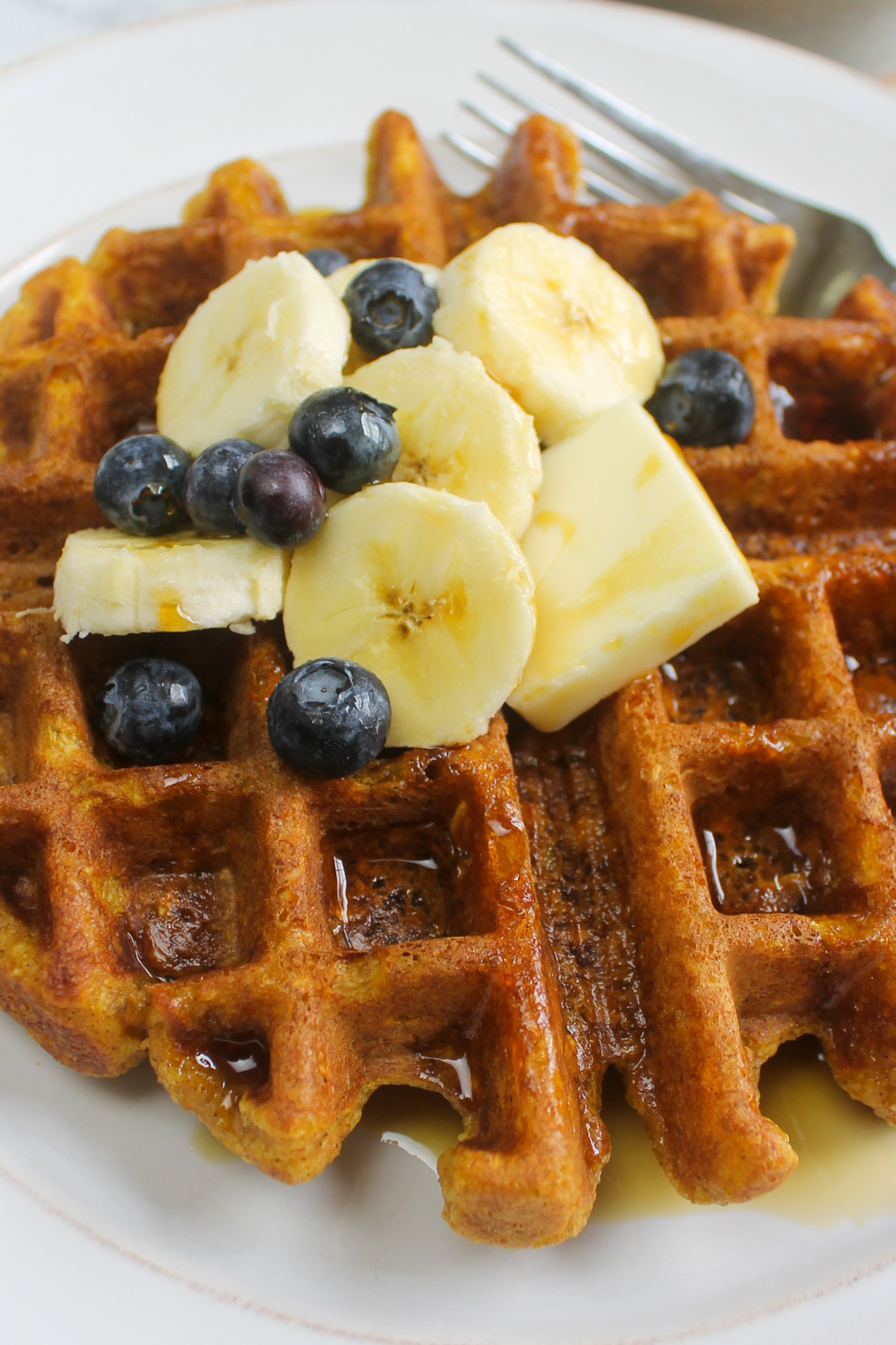 Close up of orange colored pumpkin waffles with bananas and blueberries.