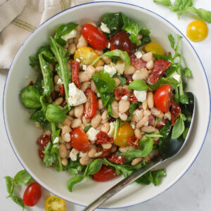 A bowl of white bean salad with sun-dried tomatoes, arugula and feta.