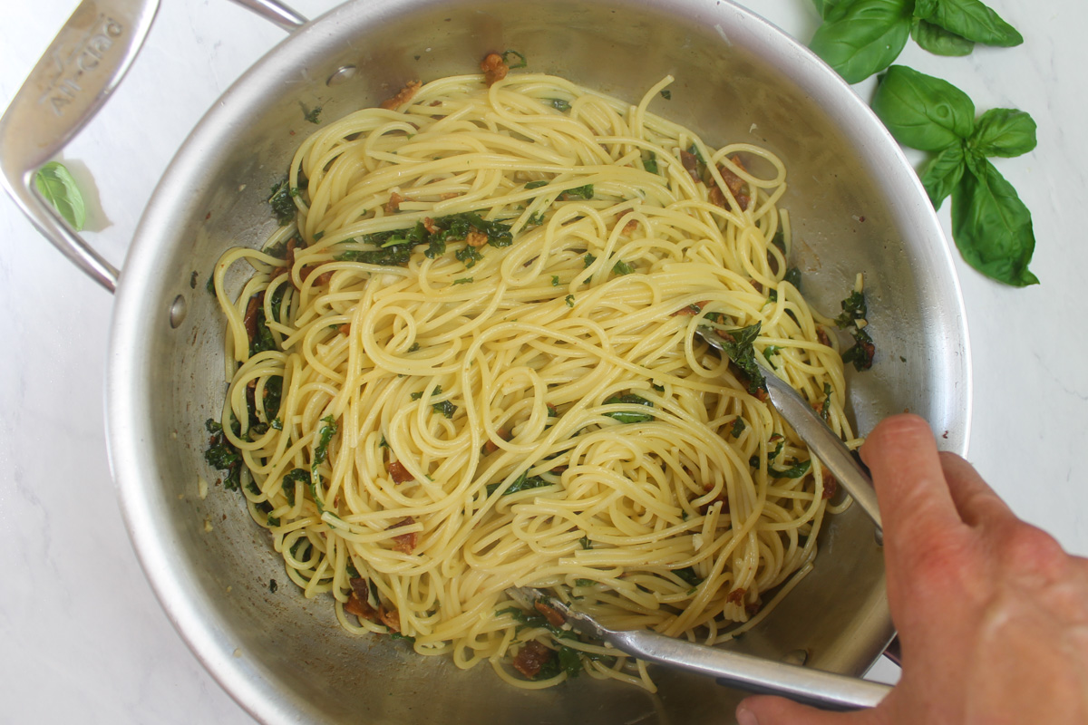 Adding the spaghetti and tossing the pasta with kale sauce with tongs.