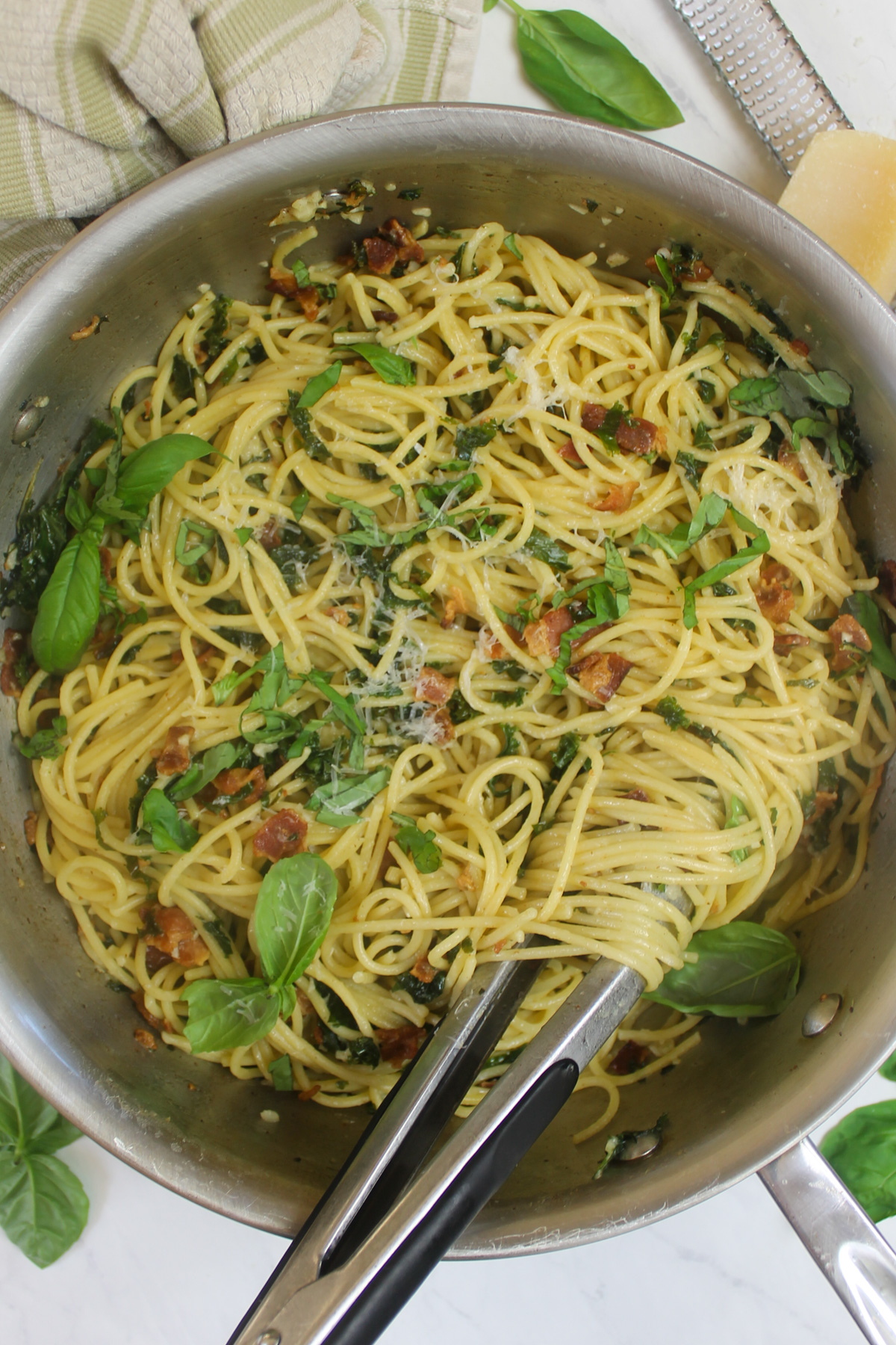 Bacon kale pasta served with tongs.