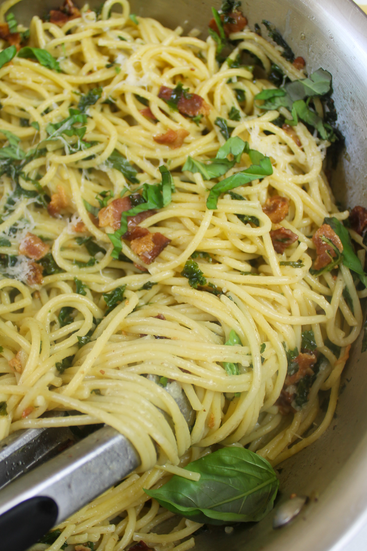 Bacon kale pasta twirled with tongs.