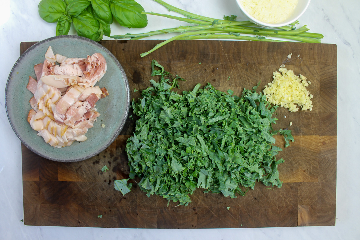 Ingredients prepped on a cutting board, sliced bacon, chopped kale and garlic.