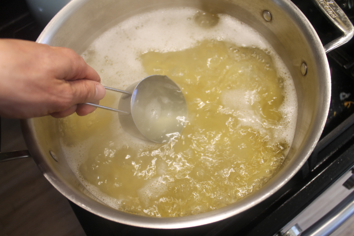 Using a measuring cup to dip into the boiling pasta water to use the starchy liquid for the sauce.