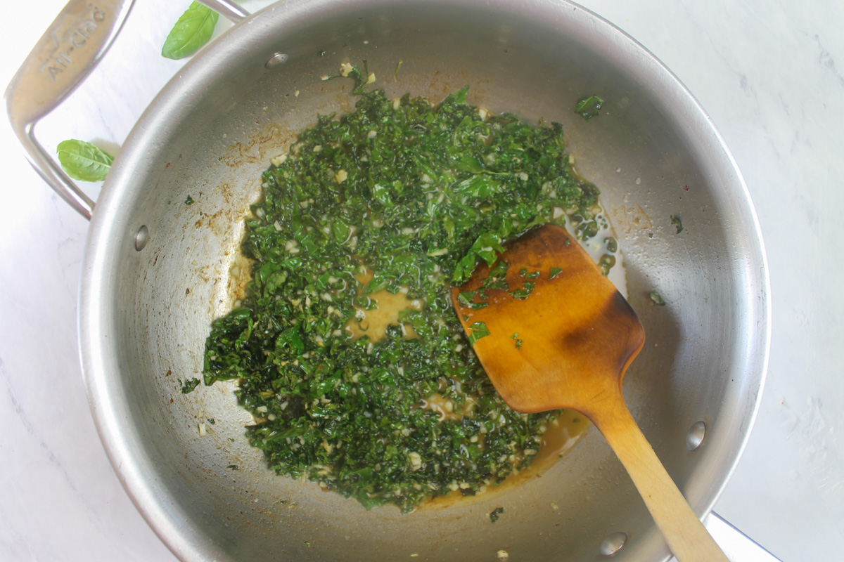 Forming the kale pasta sauce by adding starchy pasta water to the kale and garlic.