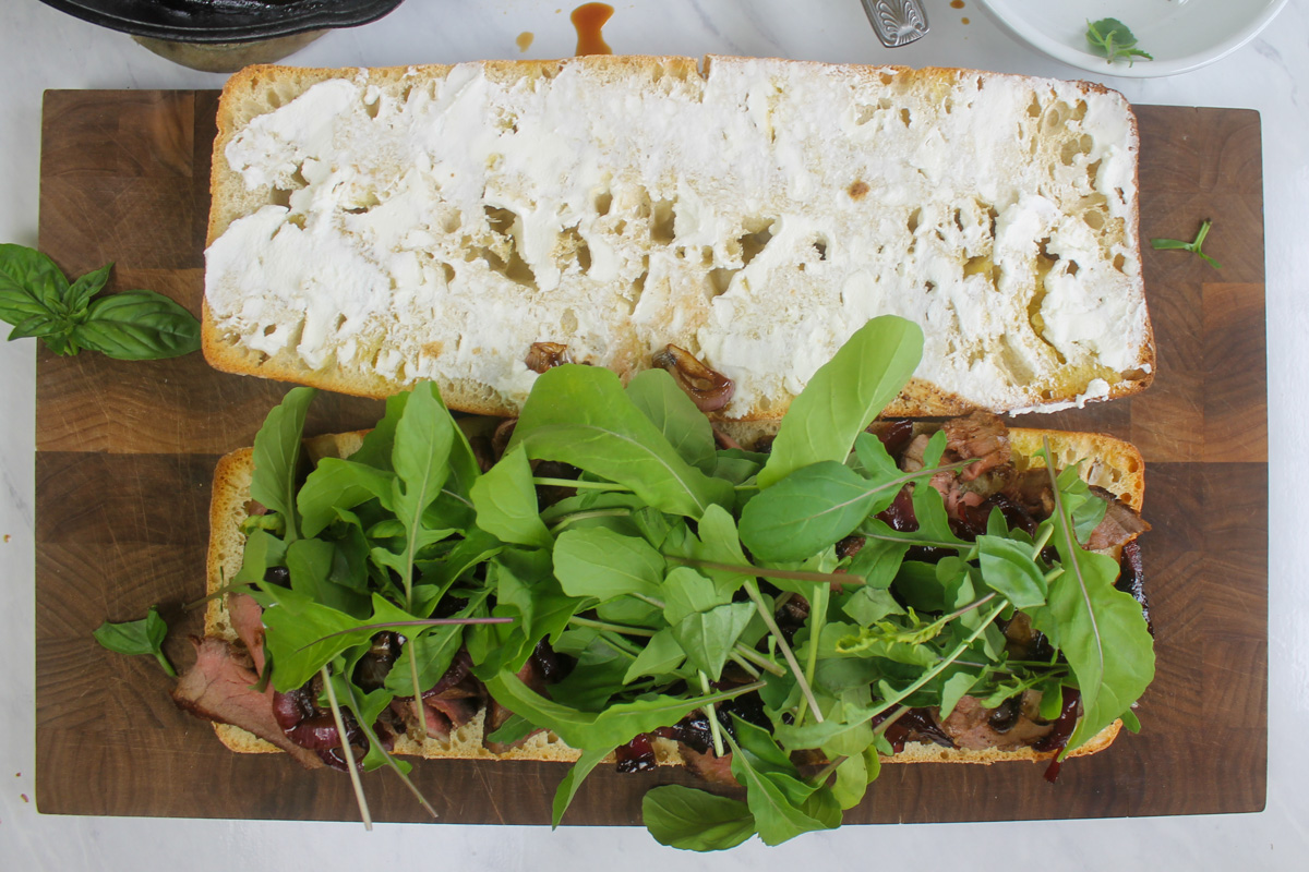 The opened steak sandwich topped with arugula and basil.