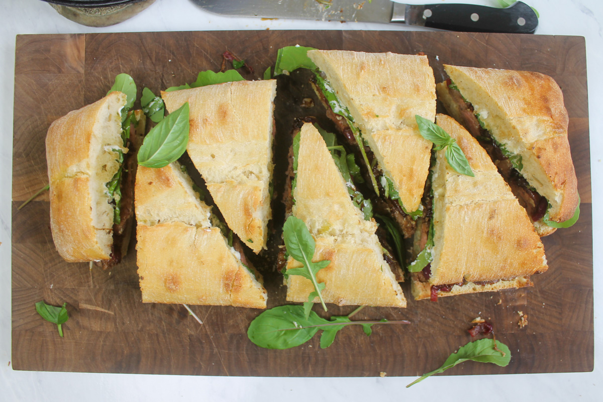 The full ciabatta sandwich sliced into triangle wedges and served on a cutting board.