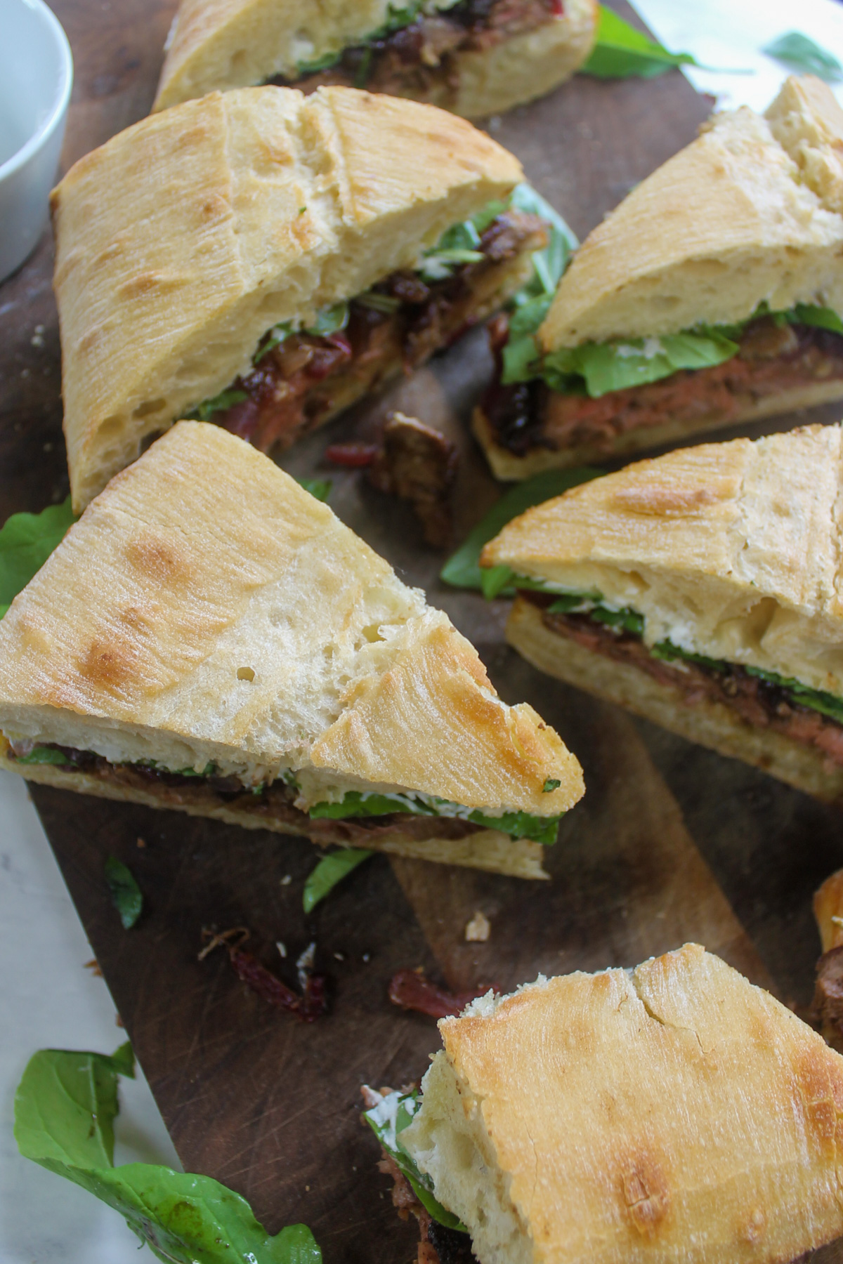 A cutting board of triangle wedges of steak sandwiches with caramelized onions.