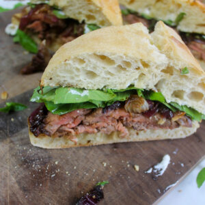 A wedge of ciabatta steak sandwich with balsamic onions and arugula.