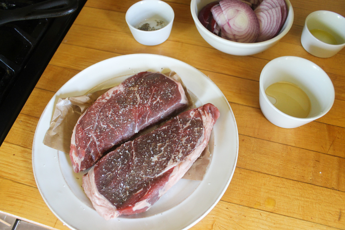 Two raw sirloin steaks on a white plate, seasoned with salt and pepper.