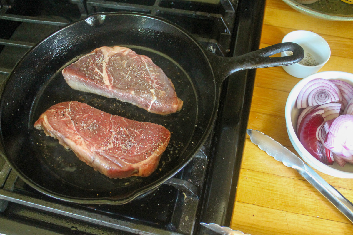 Searing the first side of the steaks in a cast iron skillet.