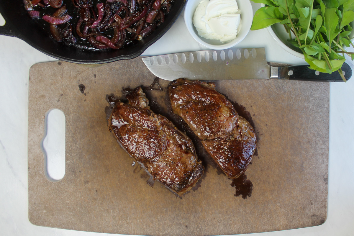 Cooked steaks resting on a cutting board before slicing.