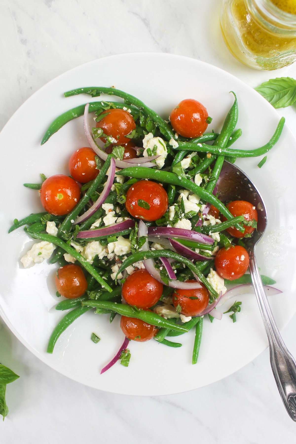 A bowl of green bean salad with tomato, feta and red onion.