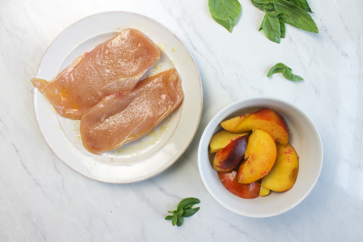 A plate of prepped raw chicken and a bowl of sliced peaches ready to grill.