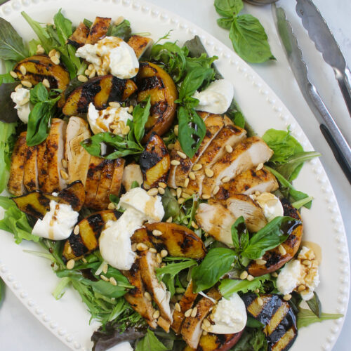 A dinner salad platter with peaches, chicken, and burrata cheese.