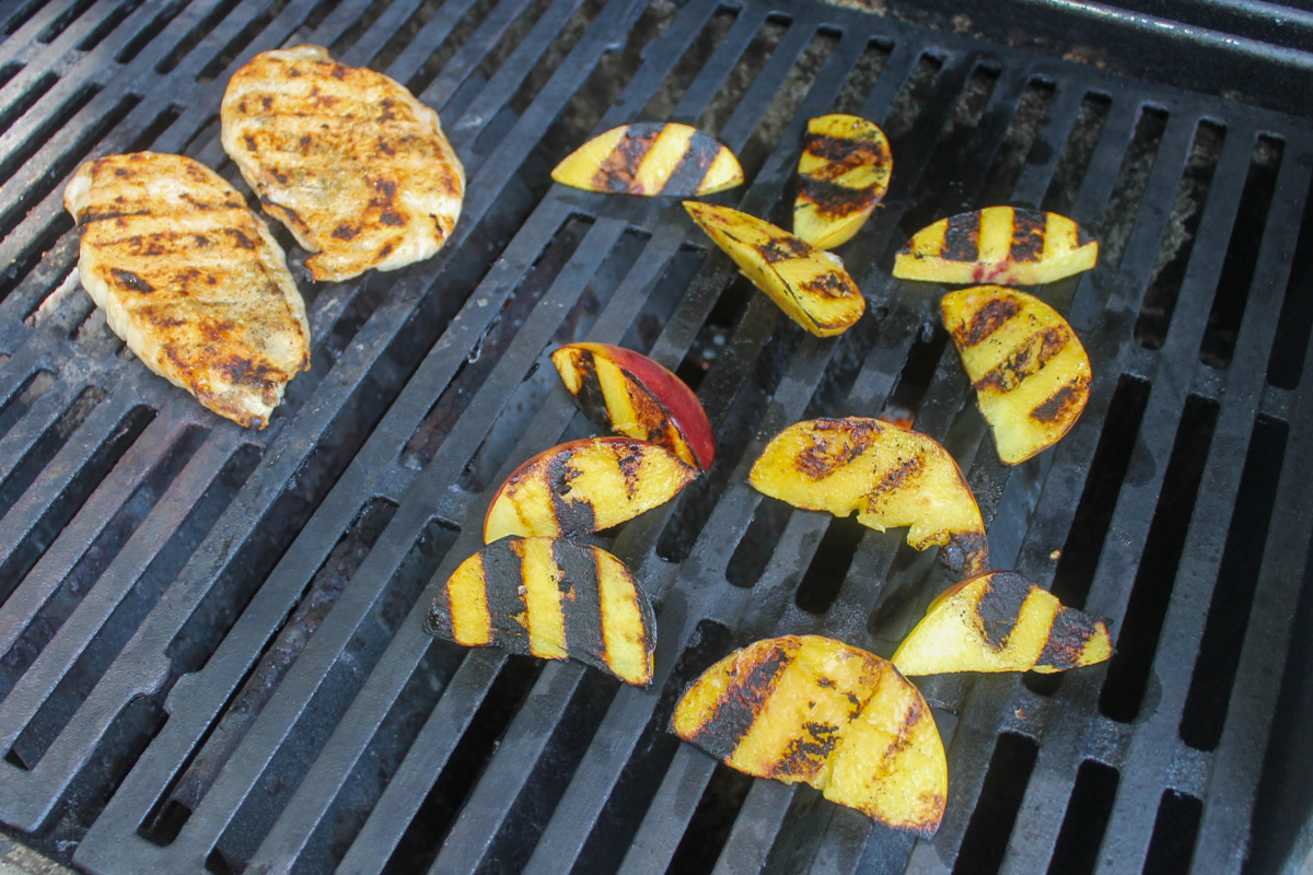 Chicken breasts and sliced peaches being grilled on an outdoor grill.