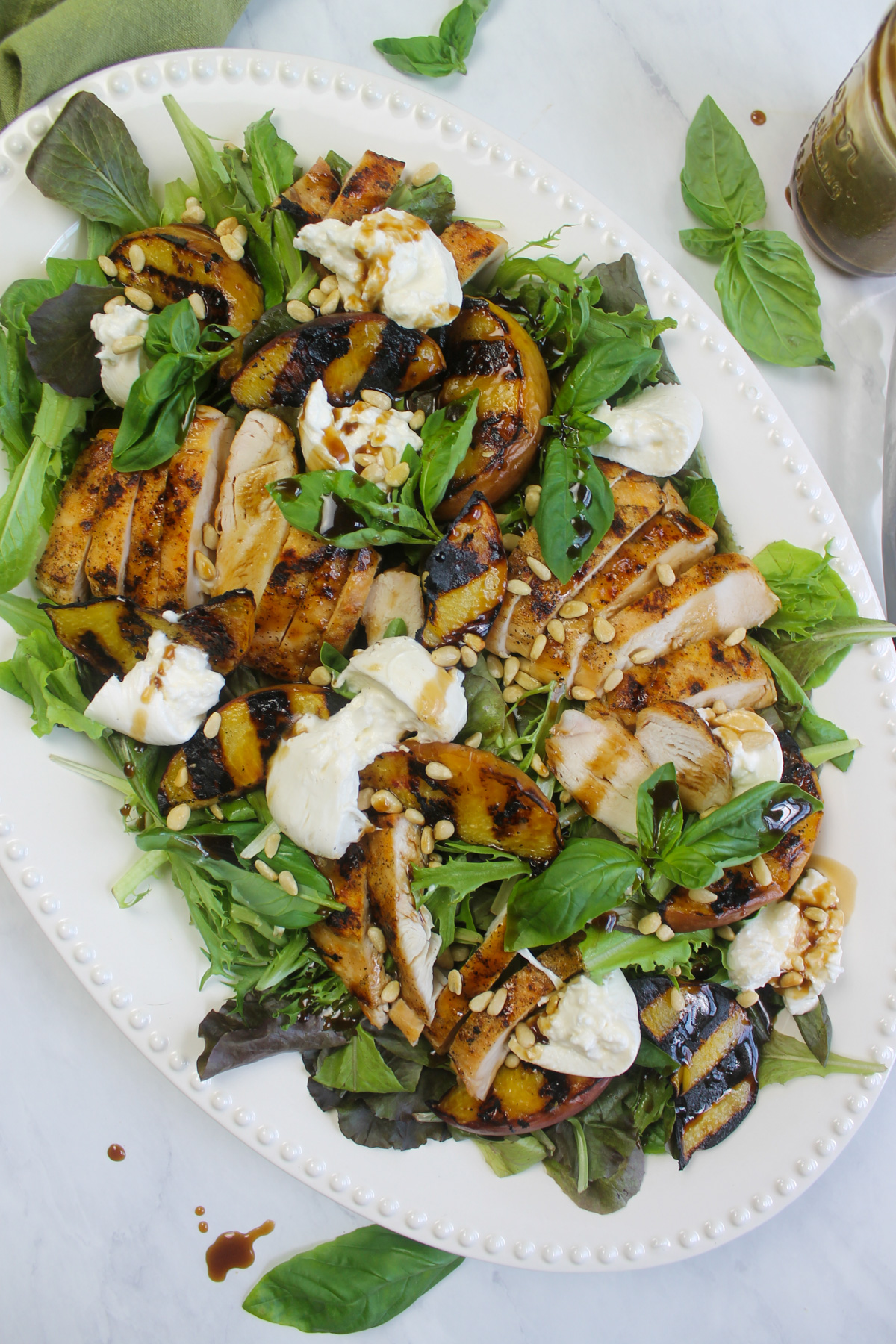 The arranged grilled peach and burrata salad on a white platter.