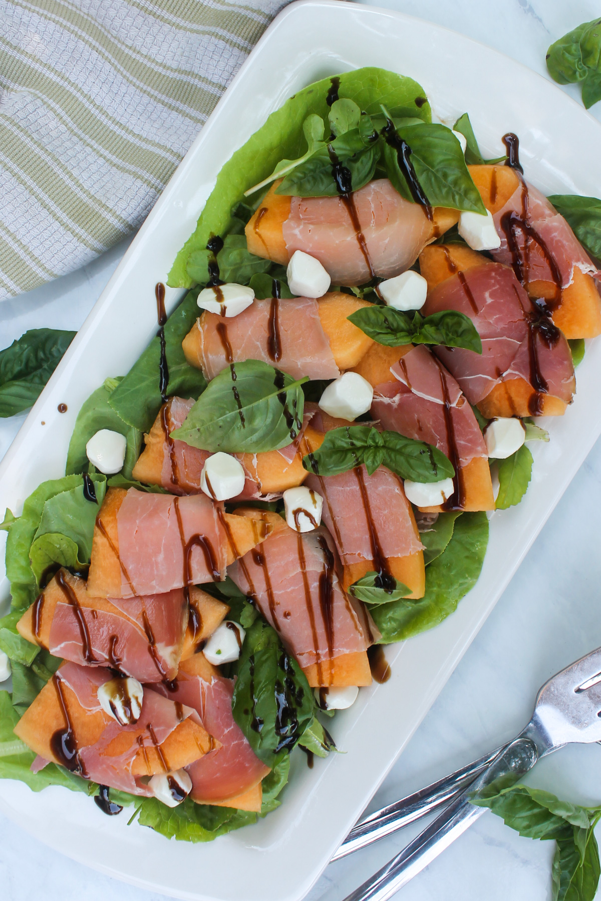 Assembled melon prosciutto salad on a bed of arugula greens with balsamic glaze.