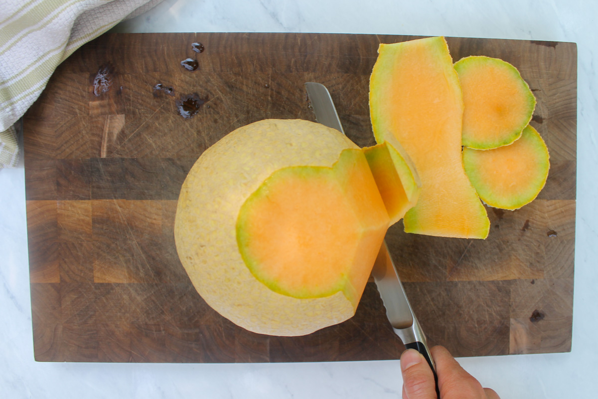 Peeling cantaloupe with a bread knife for melon prosciutto salad.