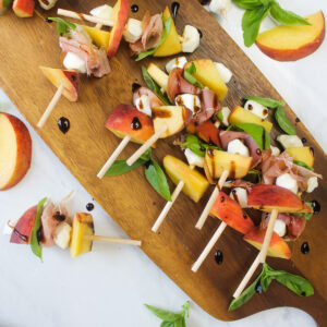 A wooden serving appetizer board of skewered peach, mozzarella, and prosciutto bites. appetizer