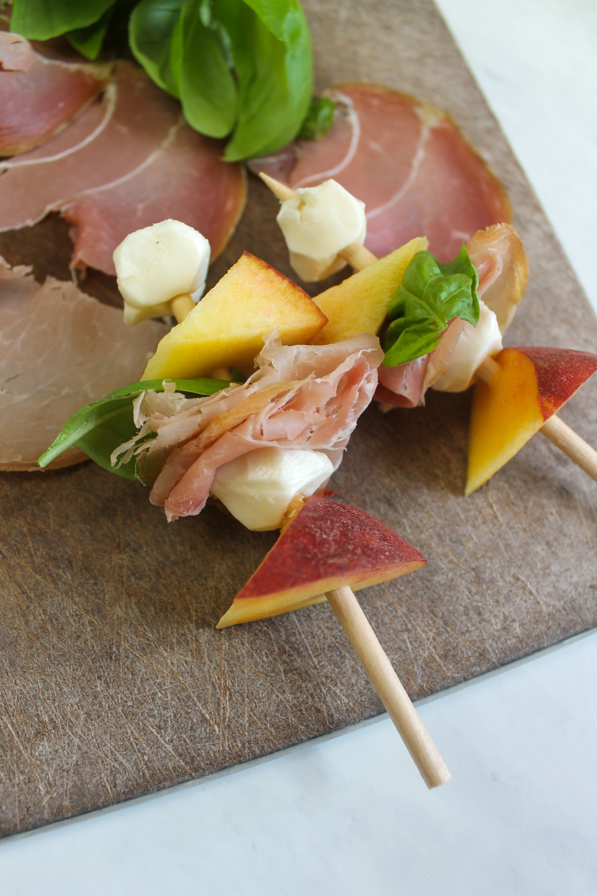 Two assembled peach caprese skewers on a cutting board.