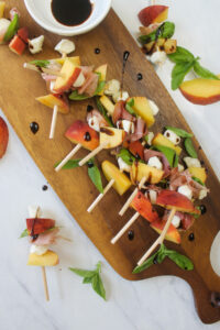 A wooden platter of peach prosciutto skewer appetizers.
