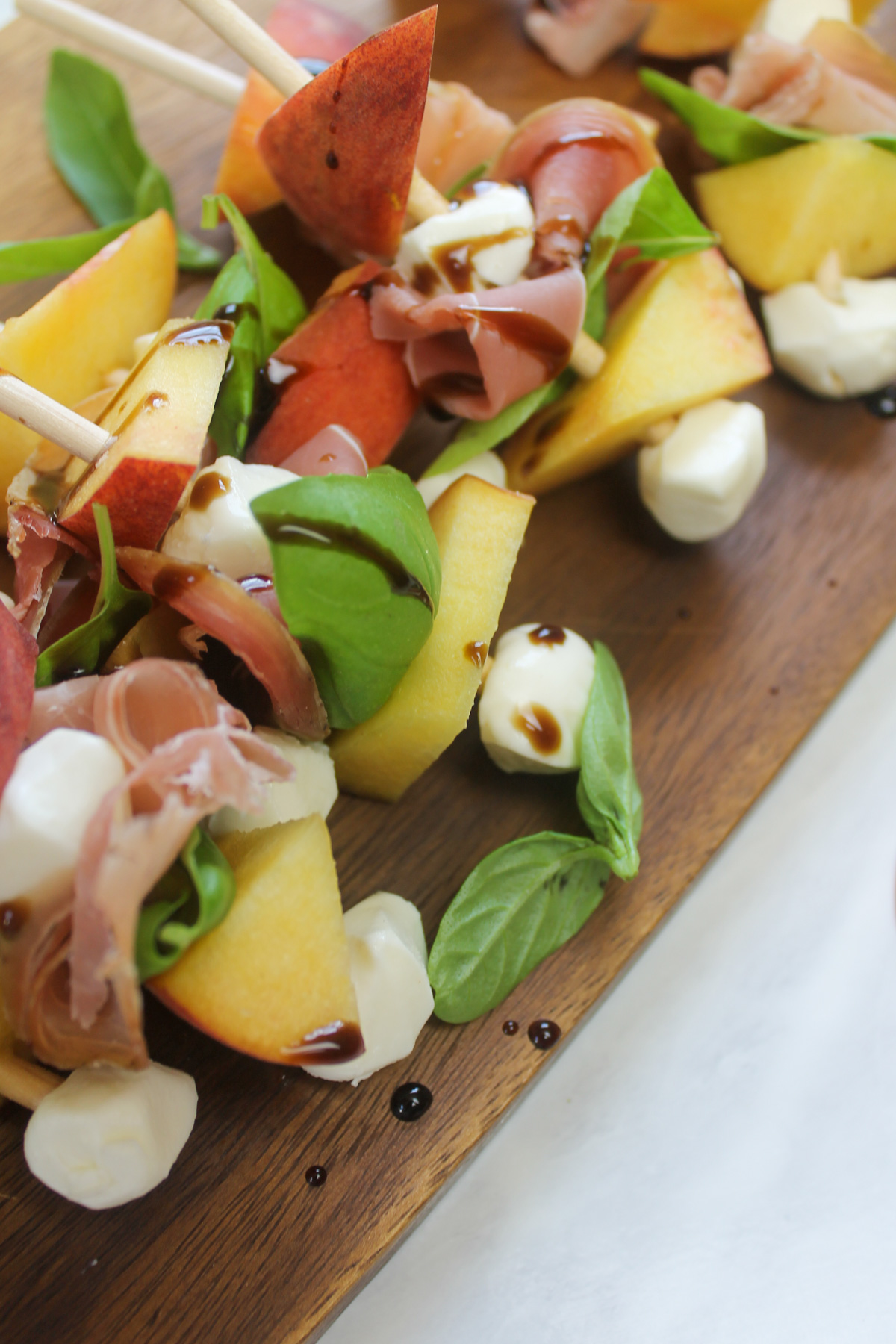 Wooden skewers with peach, mozzarella, prosciutto, basil and balsamic glaze.