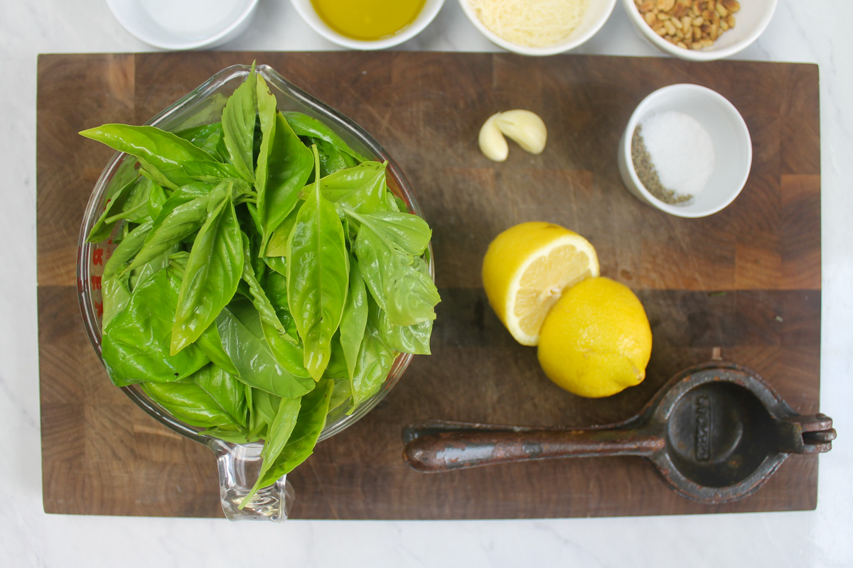Pesto ingredients on a cutting board with a glass measuring cup of 4 cups of basil and greens.