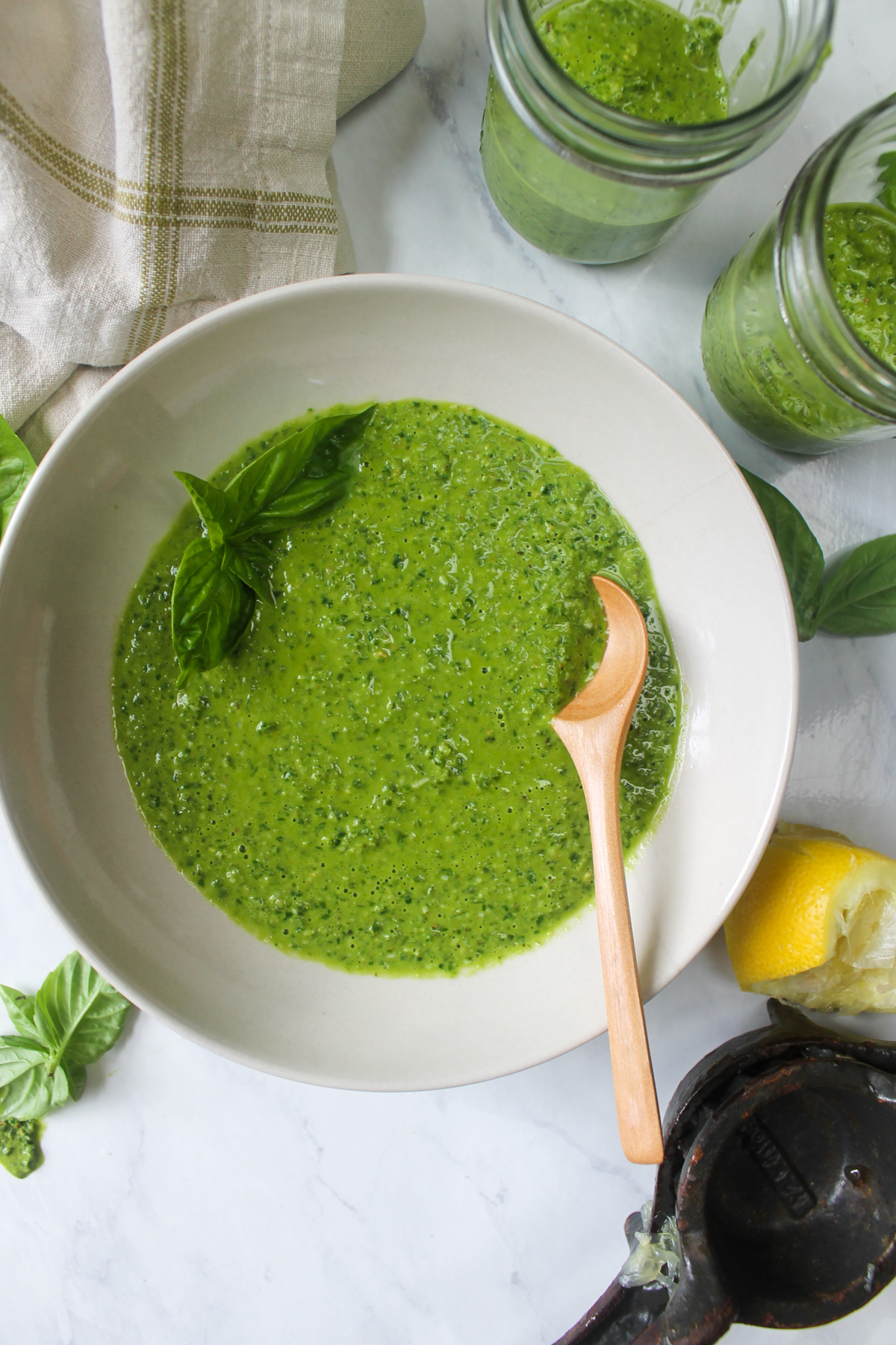 A bowl of pesto with a spoon with 2 extra jars of pesto to freeze.