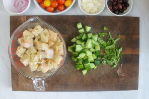 Prepped ingredients on a cutting board including 4 cups of cubed bread, chopped cucumber and basil.
