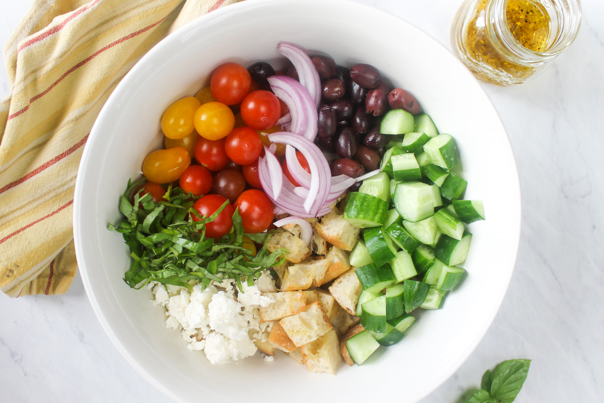 A white bowl of Panzanella ingredients ready to mix with dressing.