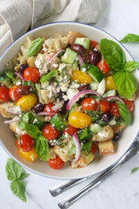 A white bowl of Panzanella bread salad with tomatoes, cucumbers and kalamata olives.