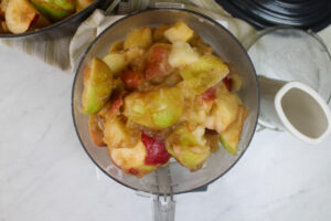 Cooked apples added to the bowl of a food processor.