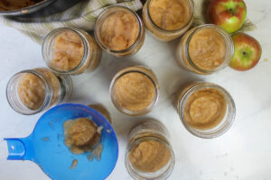 The filled jars of applesauce, using a blue jam funnel.
