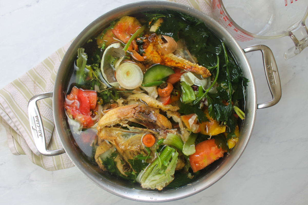 A pot of frozen chicken bones and vegetable scraps covering in water ready to make stock.